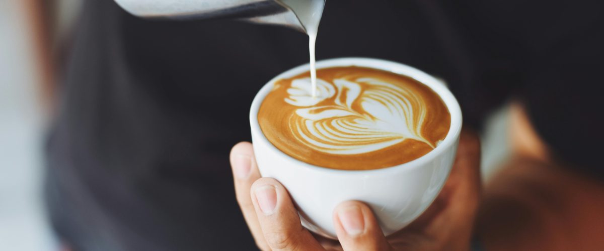 Milk being poured into a flat white coffee by a Barista