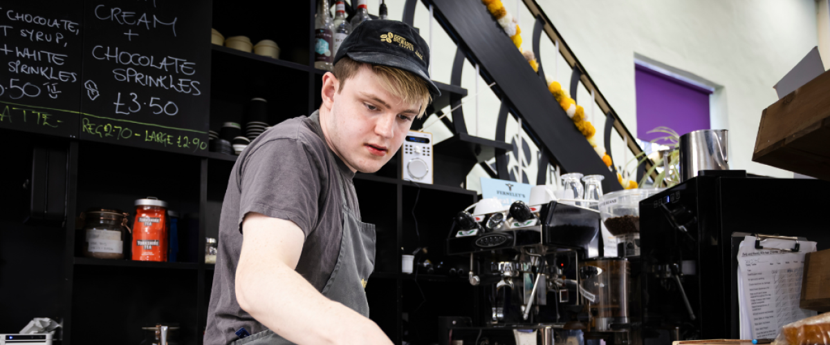 Male student wearing Brewards barista uniform and checking a visual guide before making a drink
